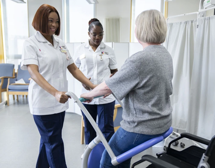 Two healthcare students assist a patient using a mobility aid in a simulated care environment. Two healthcare students assist a patient using a mobility aid in a simulated care environment.